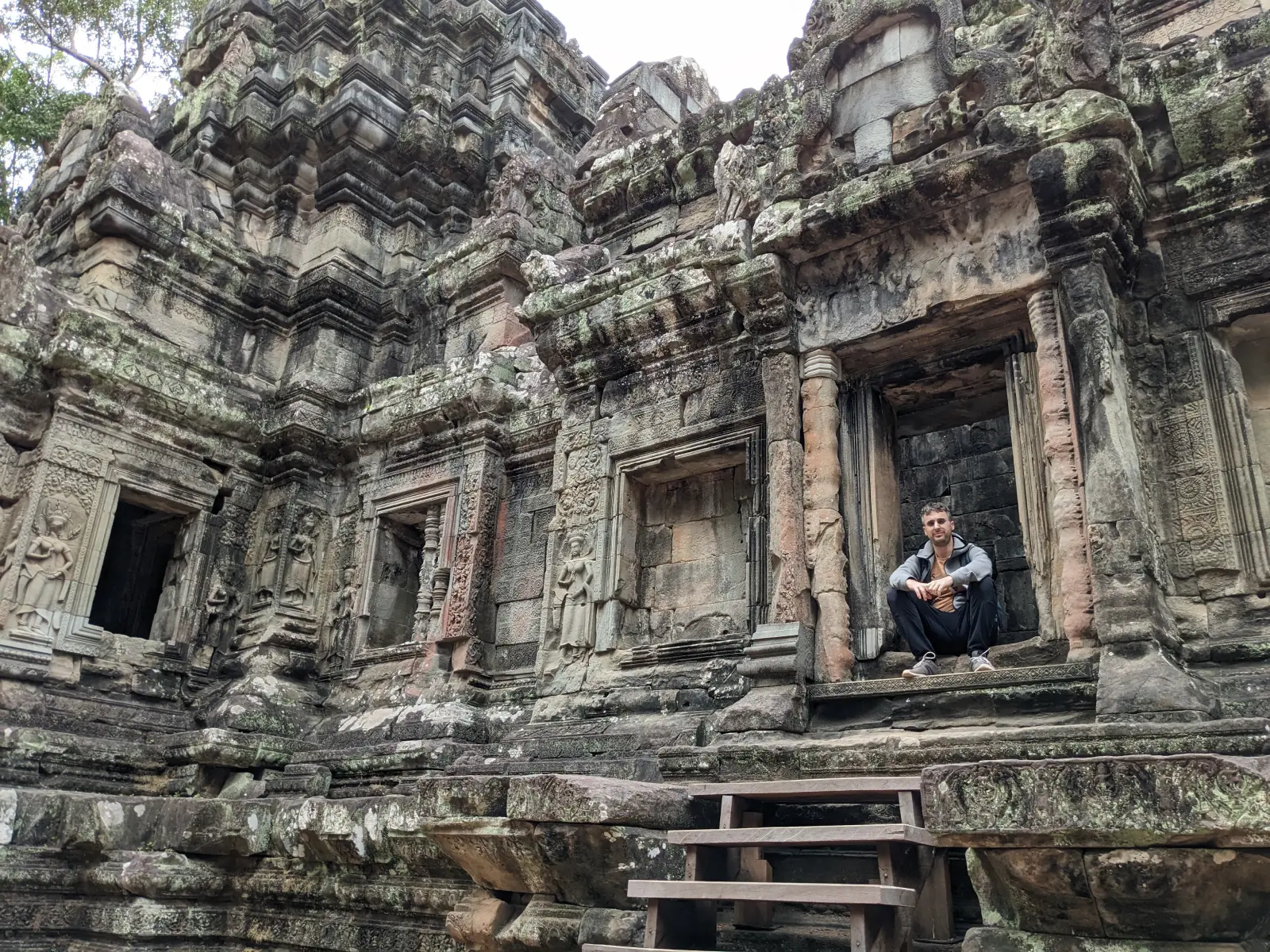 Man sitting in a doorway of an ancient stone temple with detailed carvings.