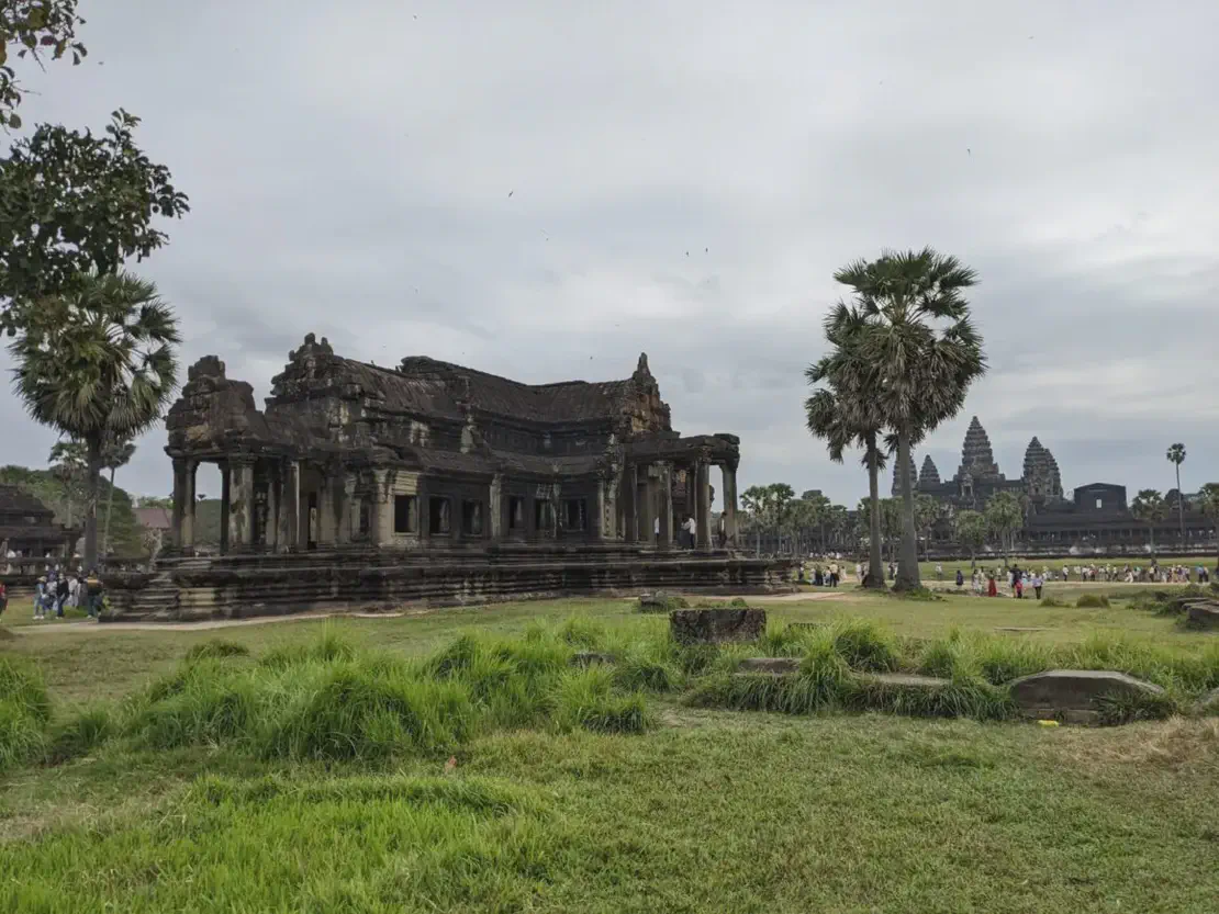 Ancient stone building at Angkor Wat with palm trees and temple towers in the background.