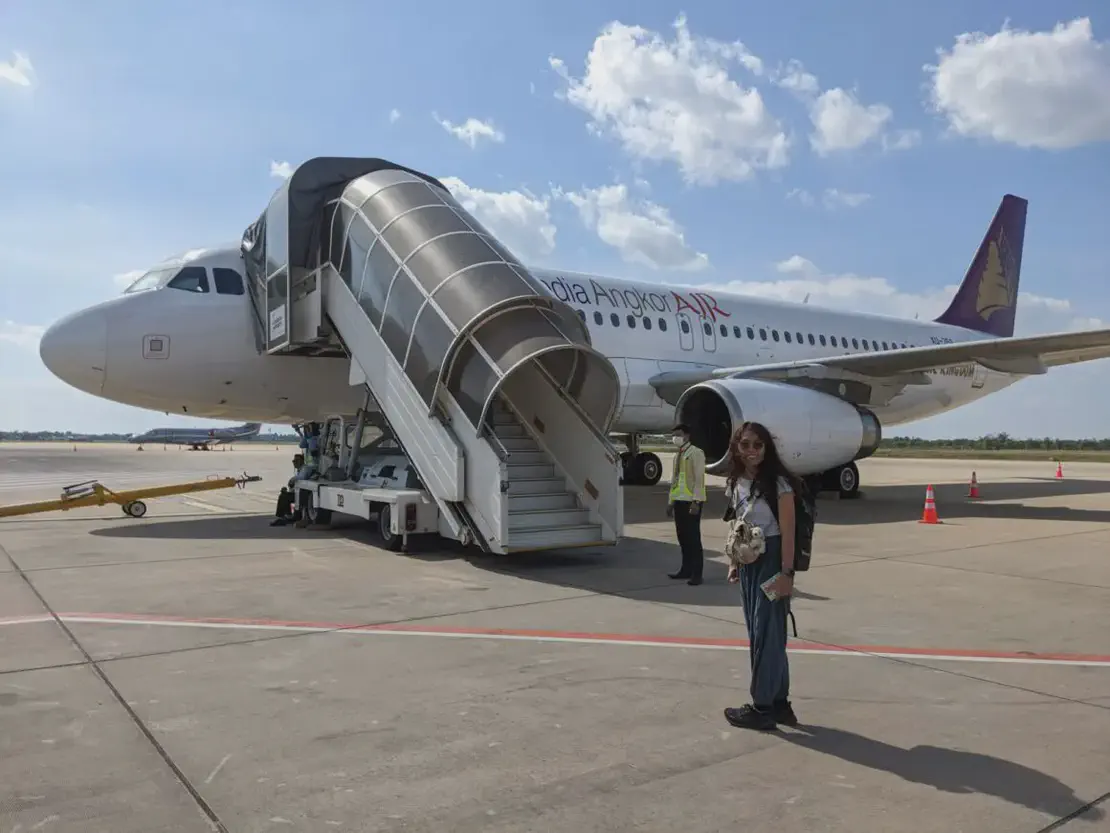 Passenger standing near a Cambodia Angkor Air plane with boarding stairs on the tarmac.