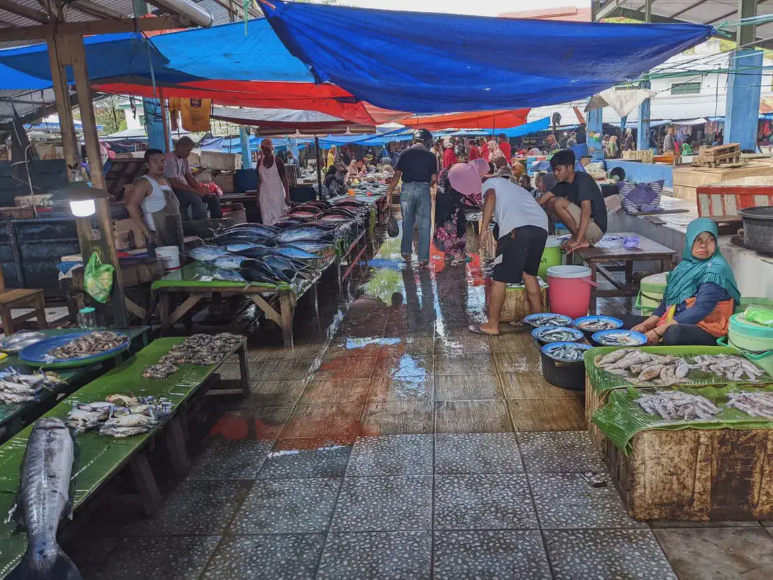 Crowded fish market with stalls displaying tuna, squid, and shrimp under blue and red tarps.