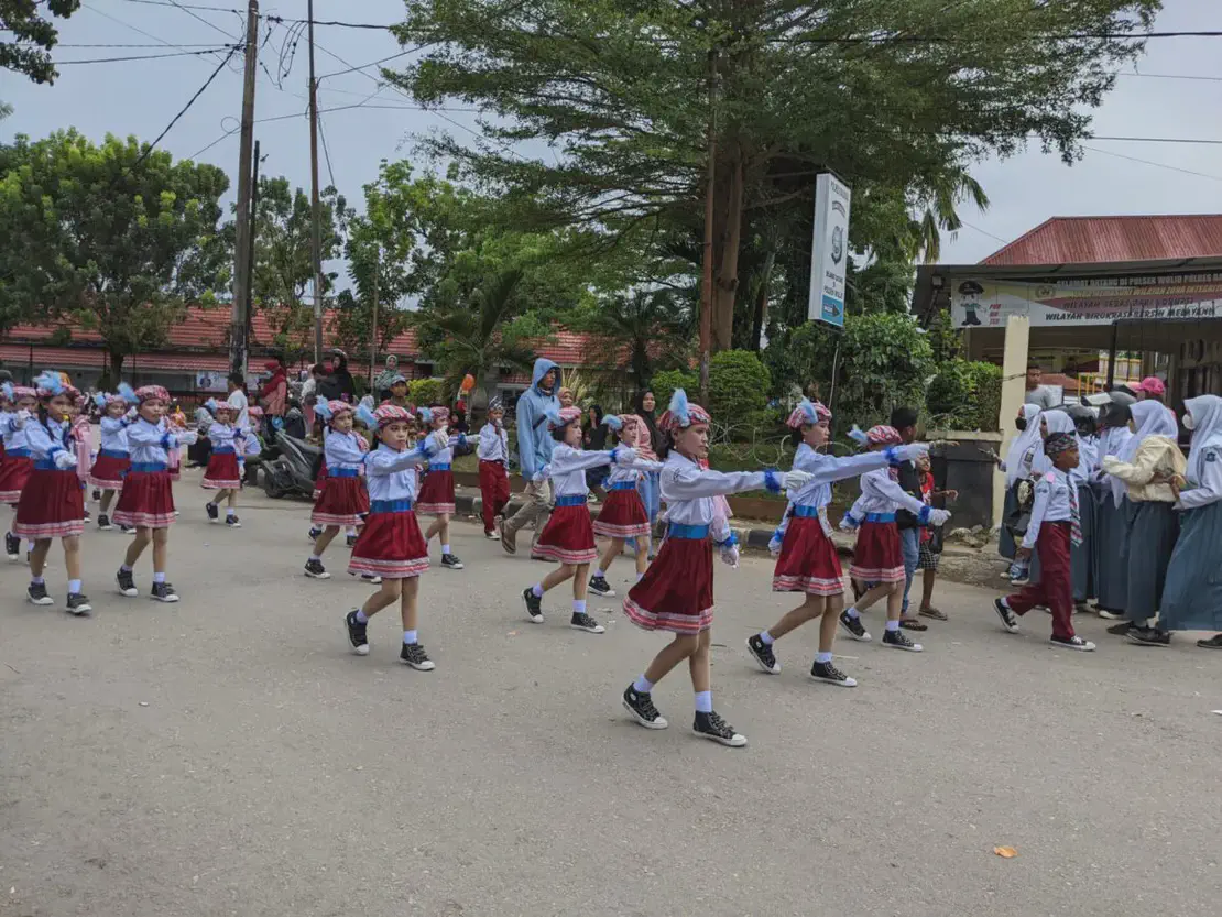Children in red skirts and white shirts marching in formation during a street parade.