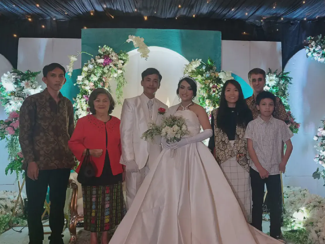 Bride in white gown and groom in white suit posing with family and friends at a wedding.