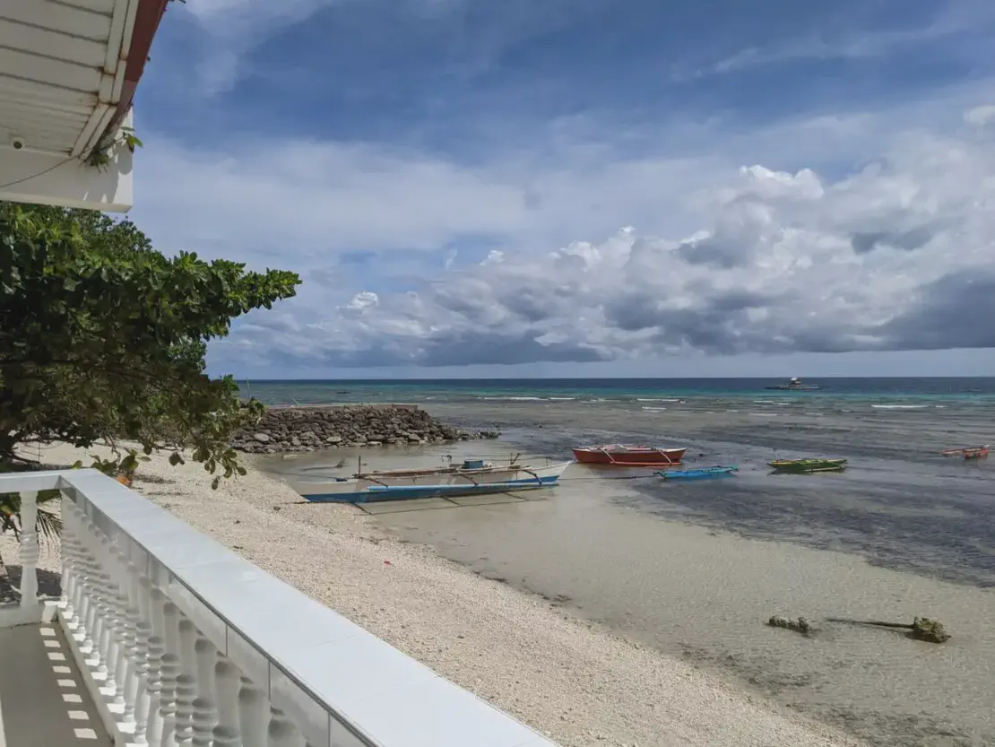 Small boats anchored on a sandy beach with a stone breakwater and cloudy sky over the ocean.