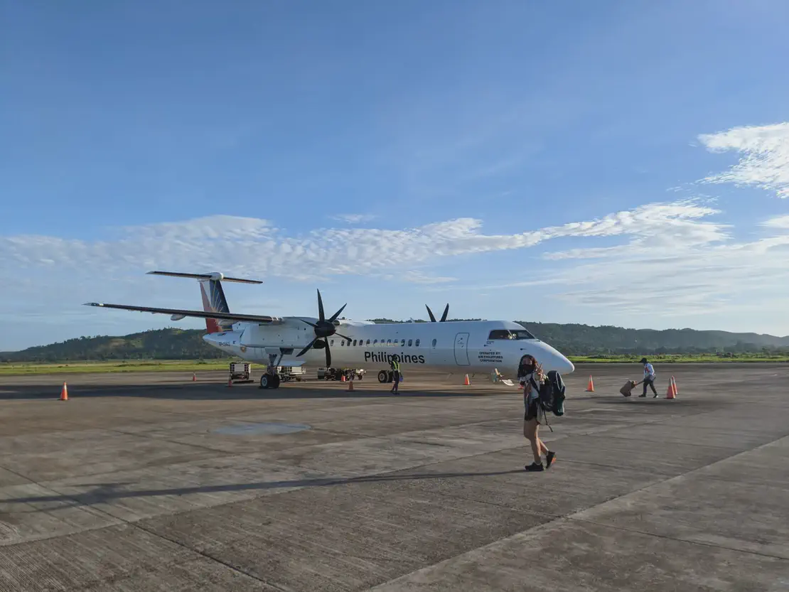 Philippine Airlines turboprop plane on an airport tarmac with passengers walking nearby.