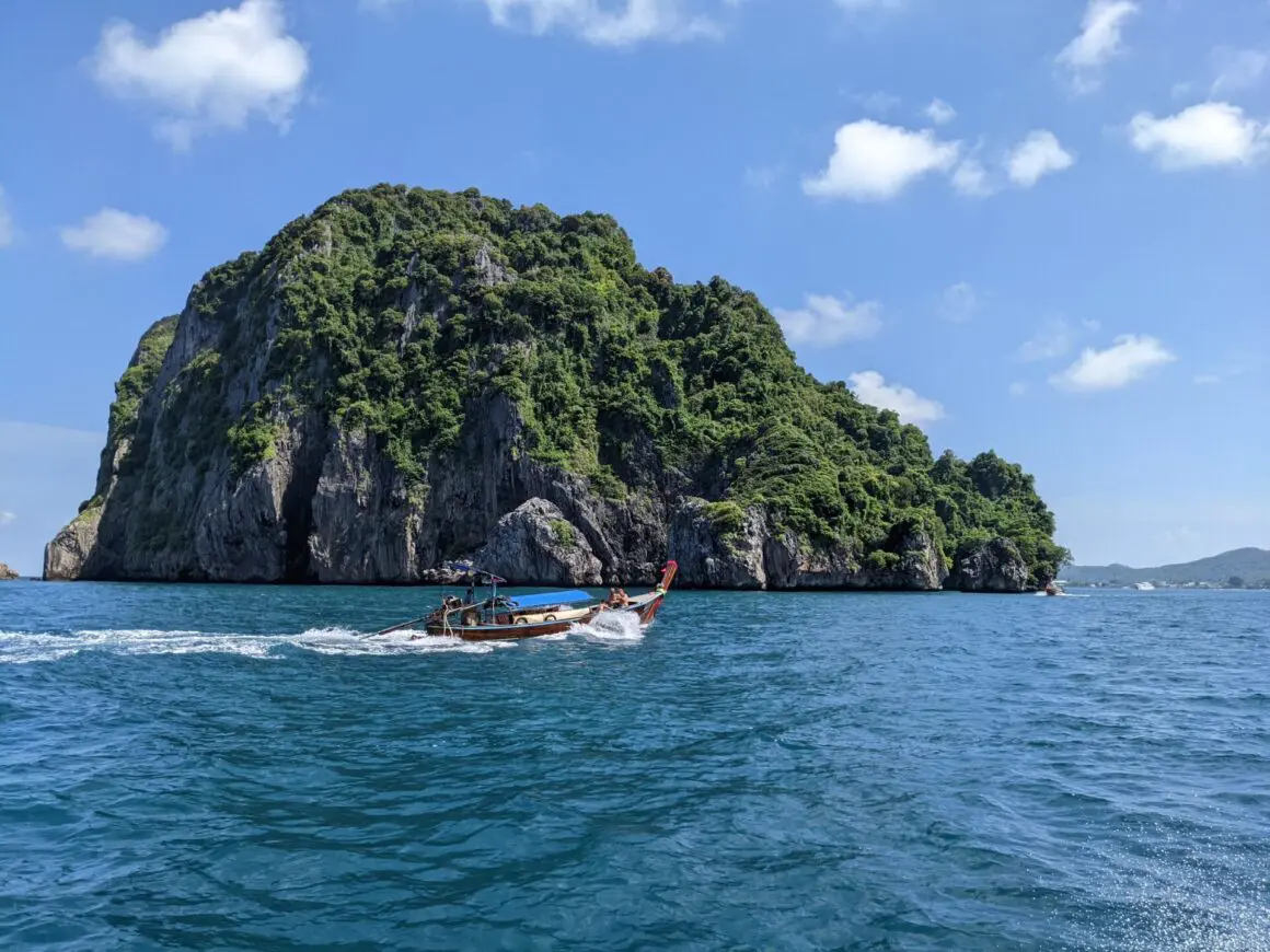 Long-tail boat speeding past a rocky island covered in green vegetation under a clear blue sky.