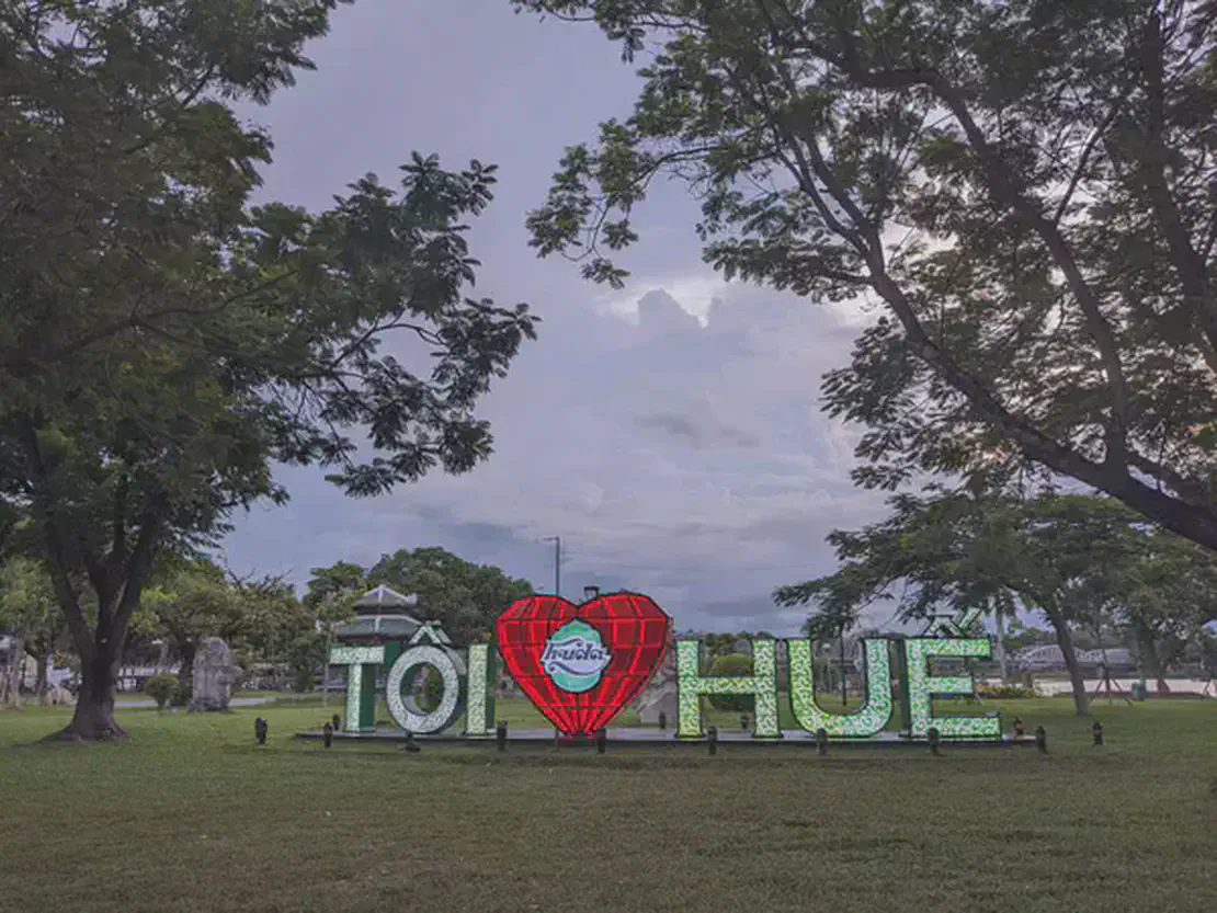 Large sign in a park reading 'Tôi yêu Huế' with a red heart symbol in the center.