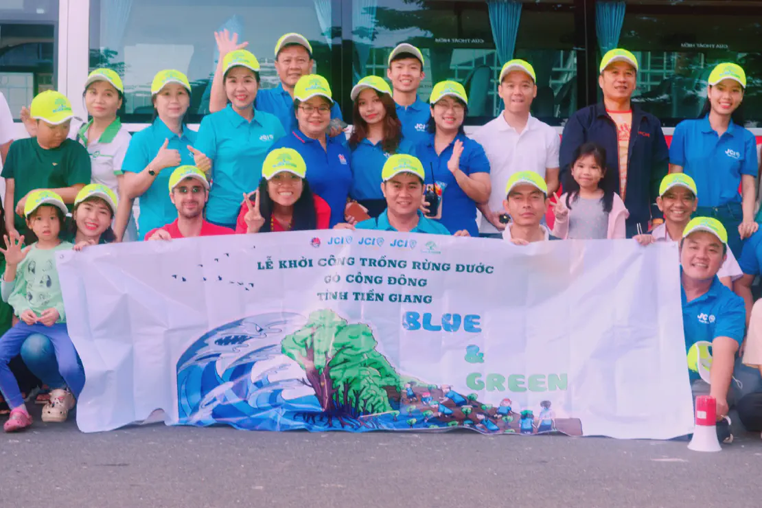 Group of people wearing bright green caps holding a banner for a community mangrove planting event in Tien Giang.