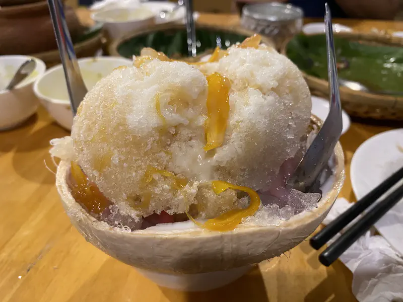 Bowl of Cambodian shaved ice dessert with syrup and fruit served in a coconut shell.