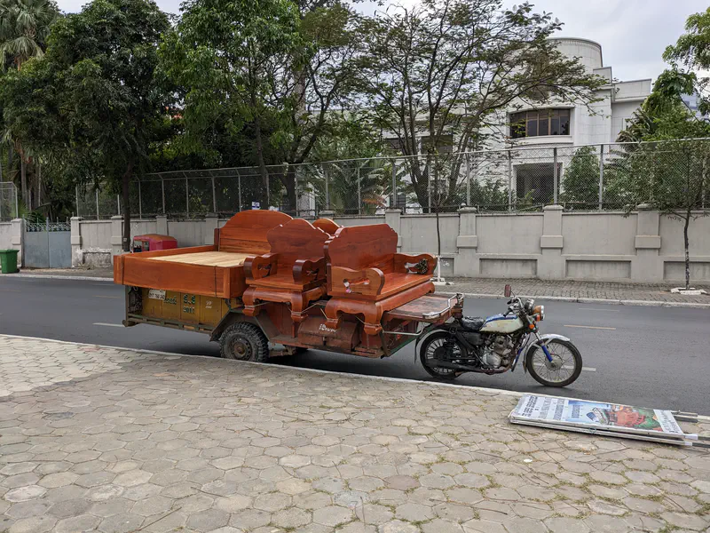 Motorbike pulling a cart loaded with large wooden furniture pieces on a city street.