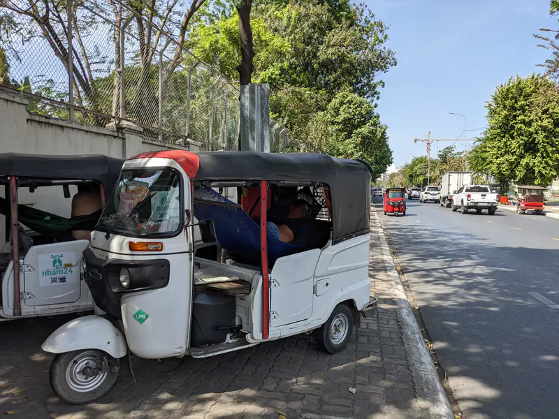 Tuk-tuks parked on the roadside, with drivers resting inside under the shade.