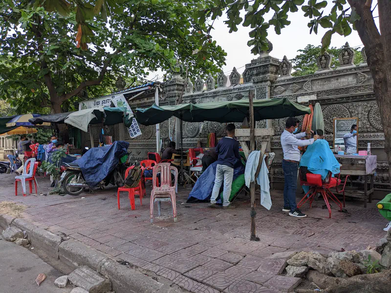 Barbers cutting hair under umbrellas at an outdoor sidewalk salon.