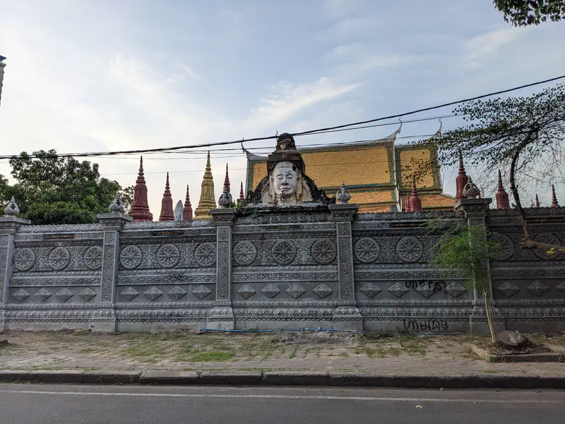 Temple wall with ornate carvings and a large Buddha face above, with colorful stupas behind.