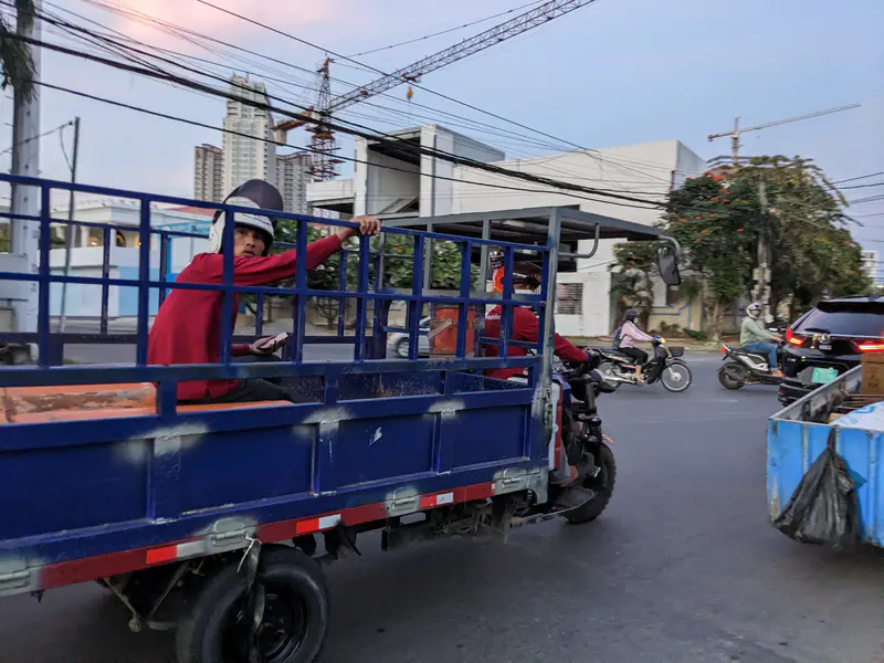 Man in a helmet riding in the back of a blue cargo tricycle on a busy street.