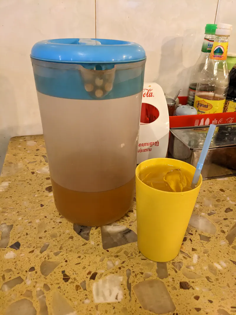 Plastic pitcher with iced tea and a yellow cup filled with the drink on a restaurant table.
