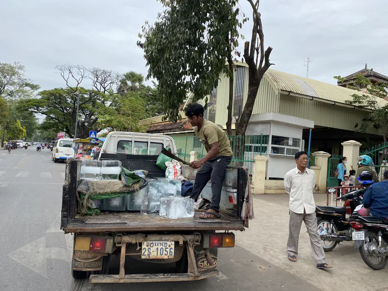 Man unloading large ice blocks from a truck on a busy street.