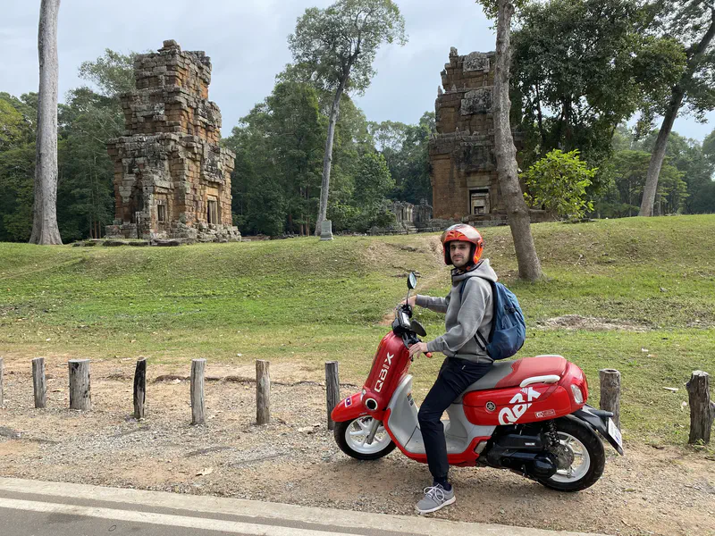 Person on a red scooter with ancient stone temple ruins in the background.