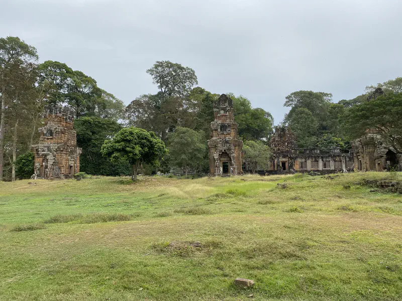 Ancient stone temple ruins with towers and walls surrounded by trees and grass.
