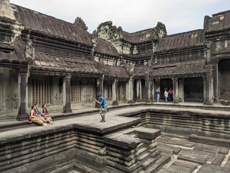 Tourists exploring an ancient courtyard with stone carvings at Angkor Wat.