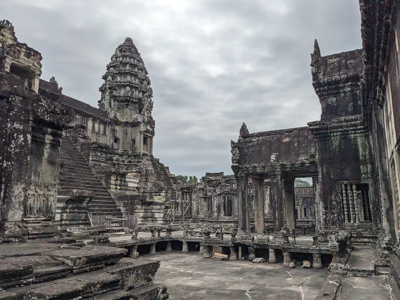 Ancient stone towers and ruins of Angkor Wat under a cloudy sky.