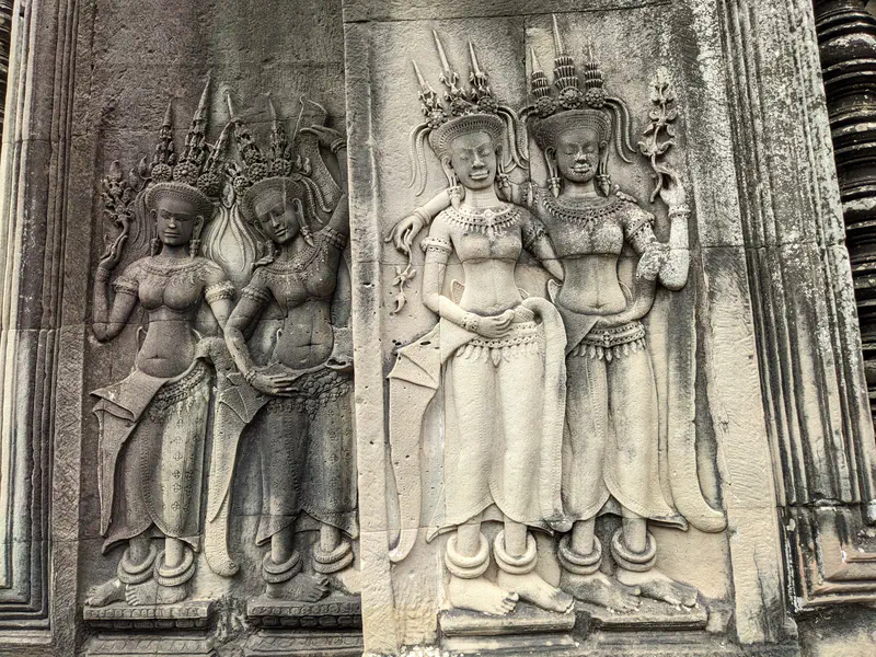 Detailed carvings of apsara dancers on a stone wall at Angkor Wat.
