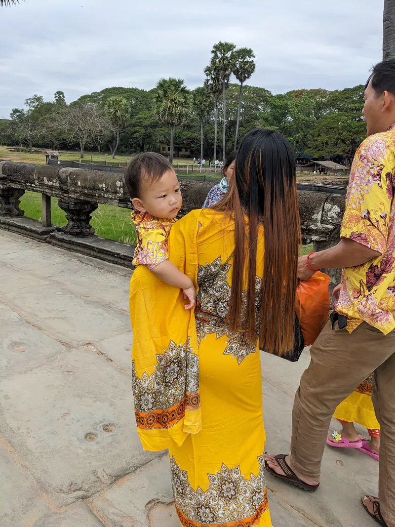 Woman in a yellow dress carrying a child in matching yellow clothing near Angkor Wat.