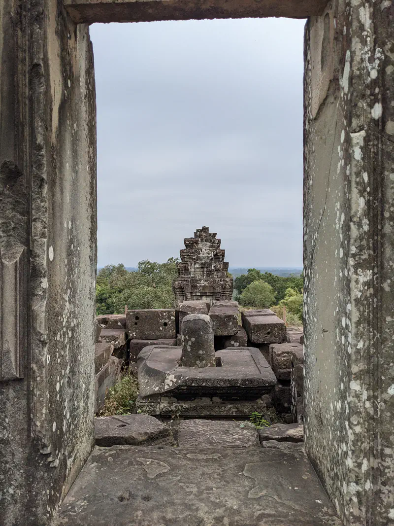 View through a stone doorway showing temple ruins and greenery in the distance.