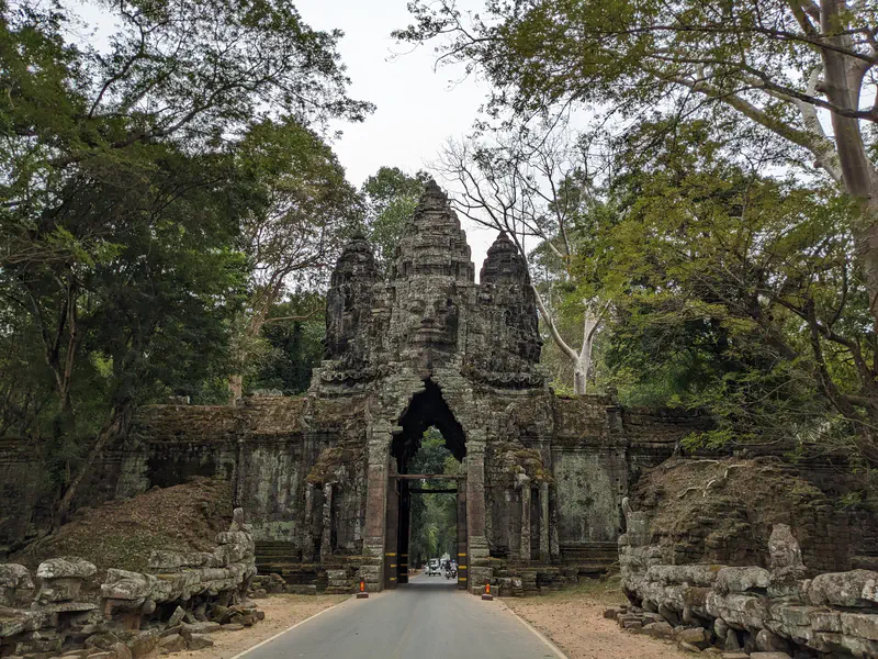 Ancient stone gate with carved faces at Angkor Thom, surrounded by trees.