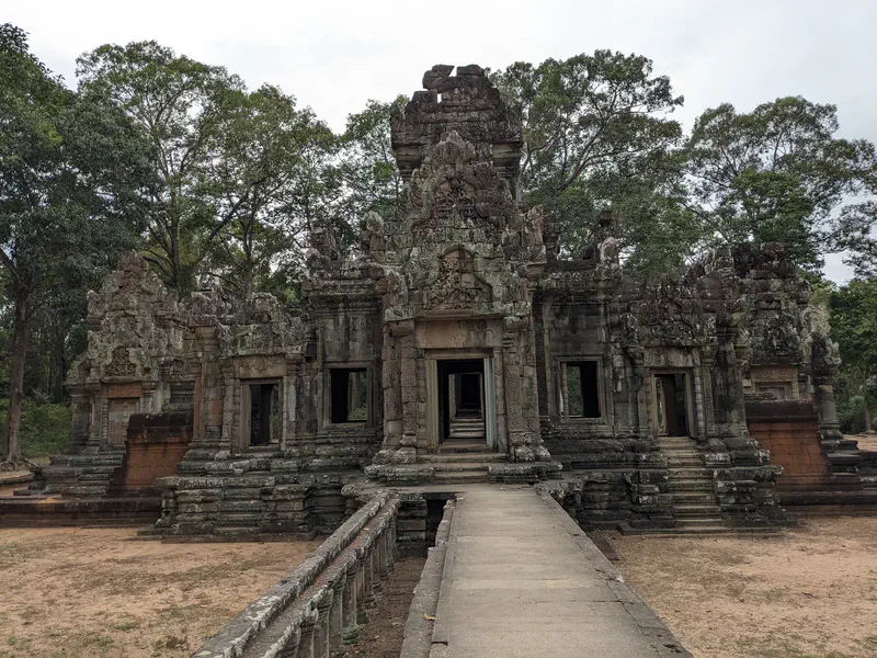 Ancient stone temple entrance with detailed carvings and stairways surrounded by trees.