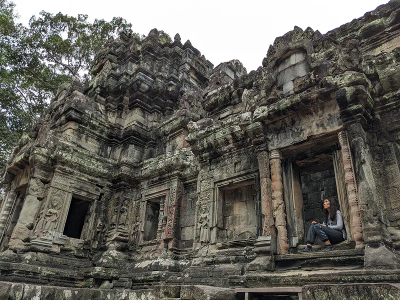 Person sitting in a doorway of an ancient stone temple with detailed carvings.
