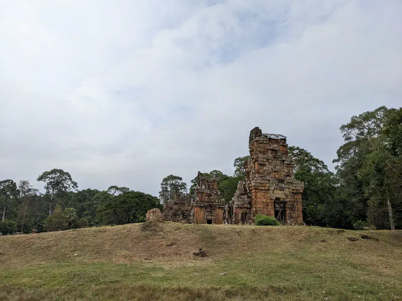 Ancient brick temple ruins standing on a grassy hill surrounded by trees.