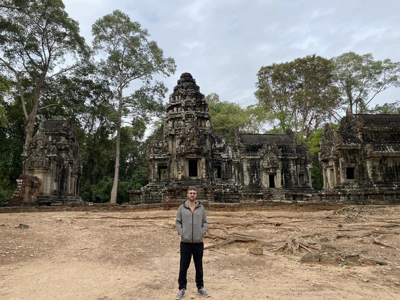 Person standing in front of ancient stone temple ruins surrounded by trees.