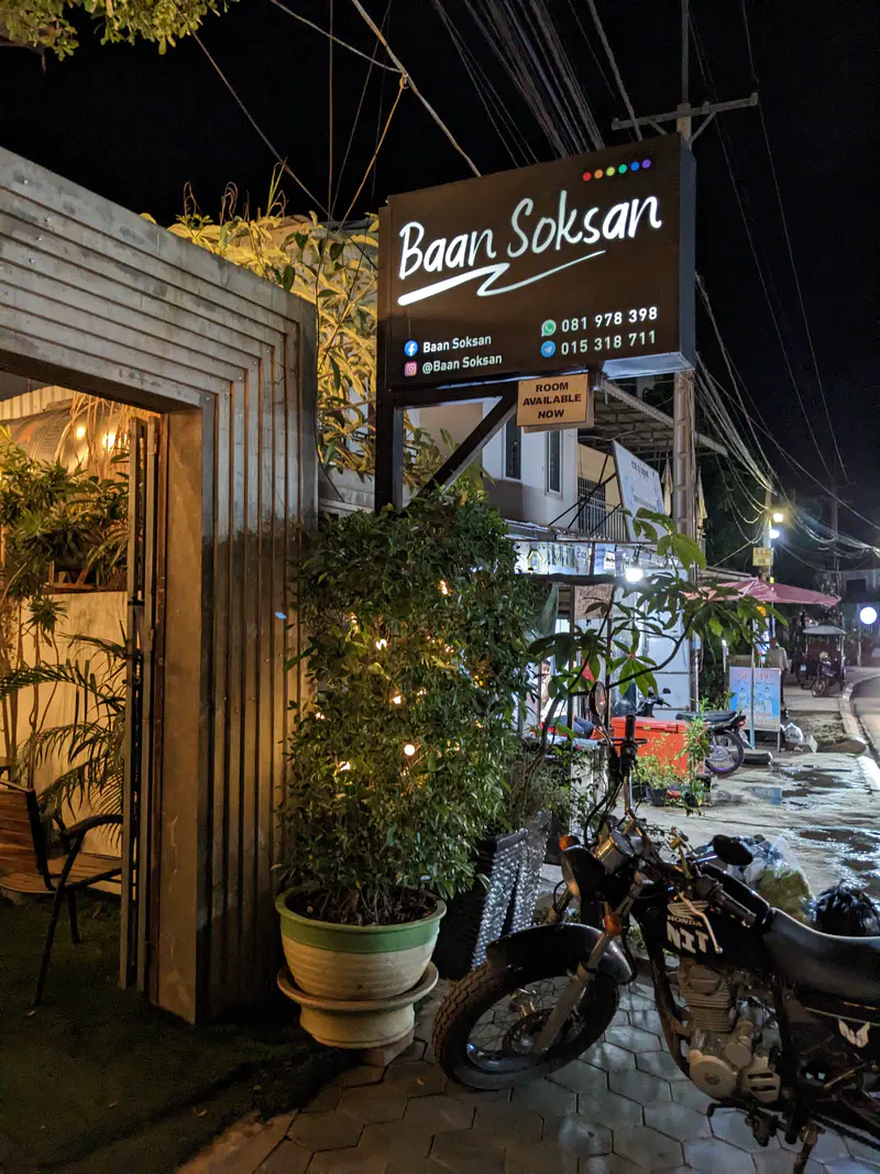 Baan Soksan guesthouse entrance with sign and parked motorcycle at night.