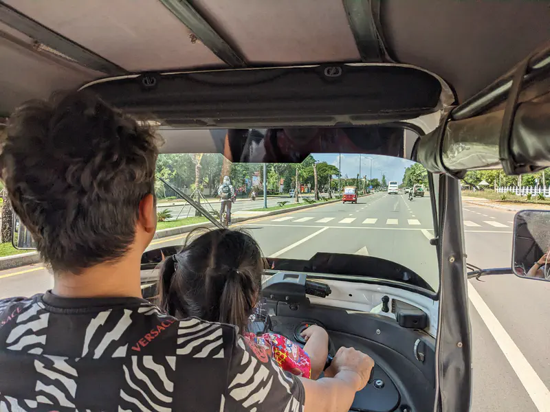 View from inside a tuk-tuk as driver and child ride along a city street.