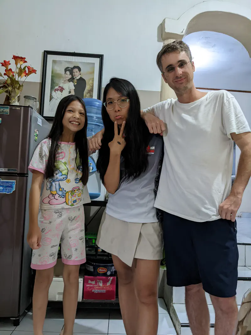 Three people posing together indoors, with a young girl in pajamas, a woman making a peace sign, and a man smiling, standing under a framed wedding photo.