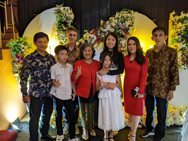 Family group photo at a formal event with floral decorations and warm lighting in the background.