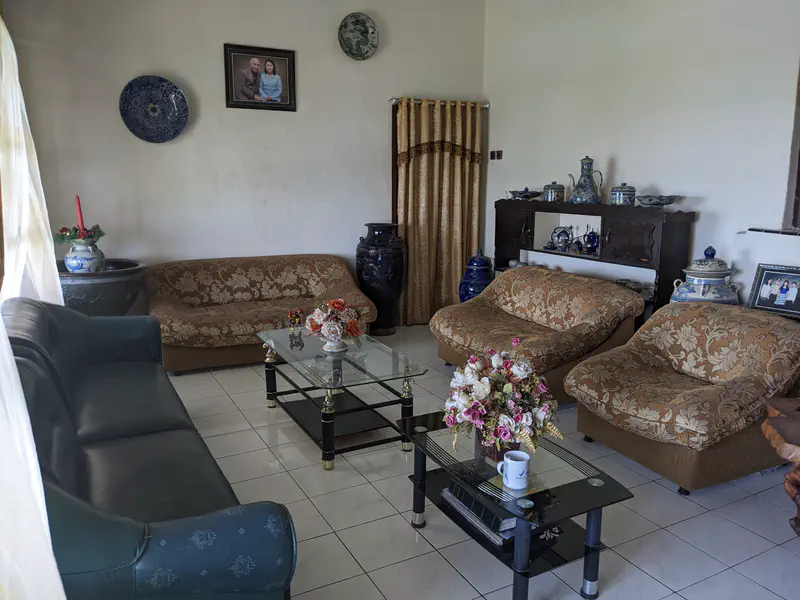 Living room with floral-patterned sofas, a dark green couch, glass coffee tables with flower arrangements, and decorative blue-and-white ceramic vases and plates.