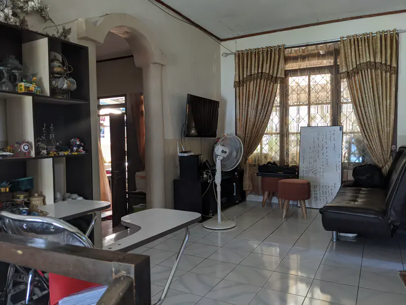 Living room with golden curtains, a TV mounted on the wall, a black sofa, a whiteboard leaning against the window, and shelves filled with collectibles and glassware.