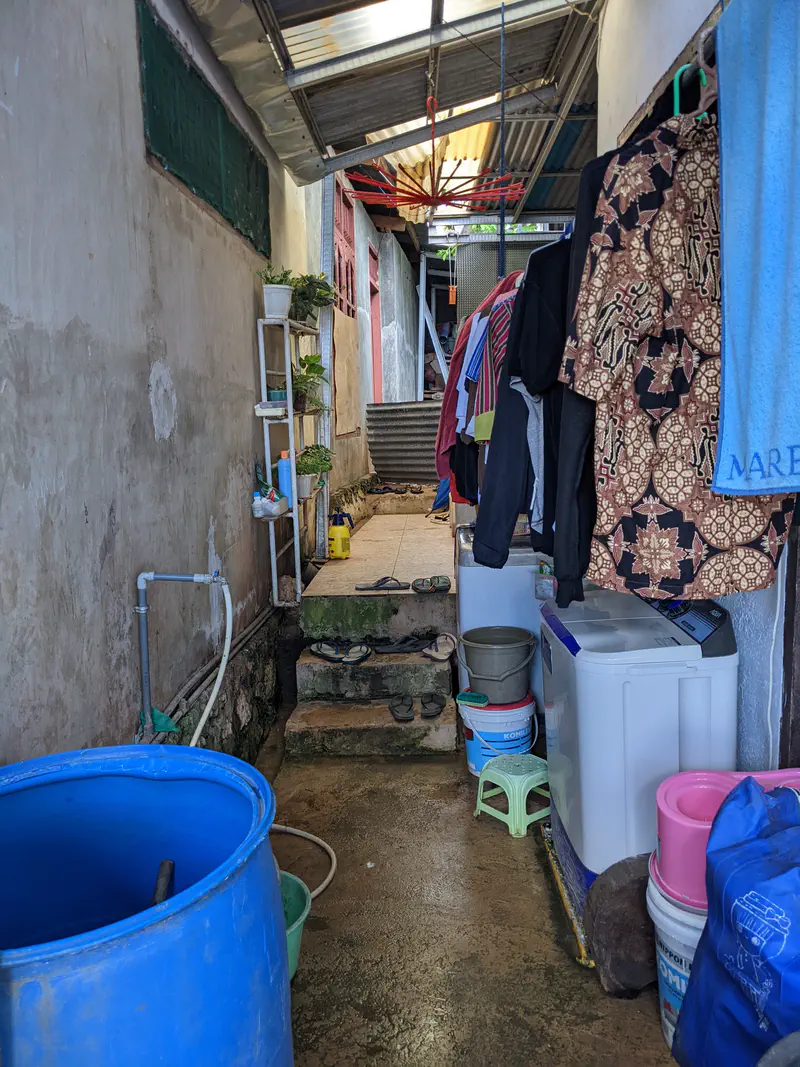 Outdoor laundry area with a washing machine, hanging clothes, water buckets, and steps leading up to another part of the house.