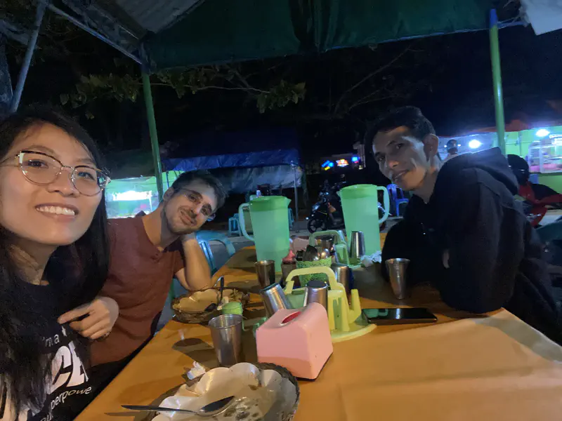 Three people sitting at a night market food stall table.