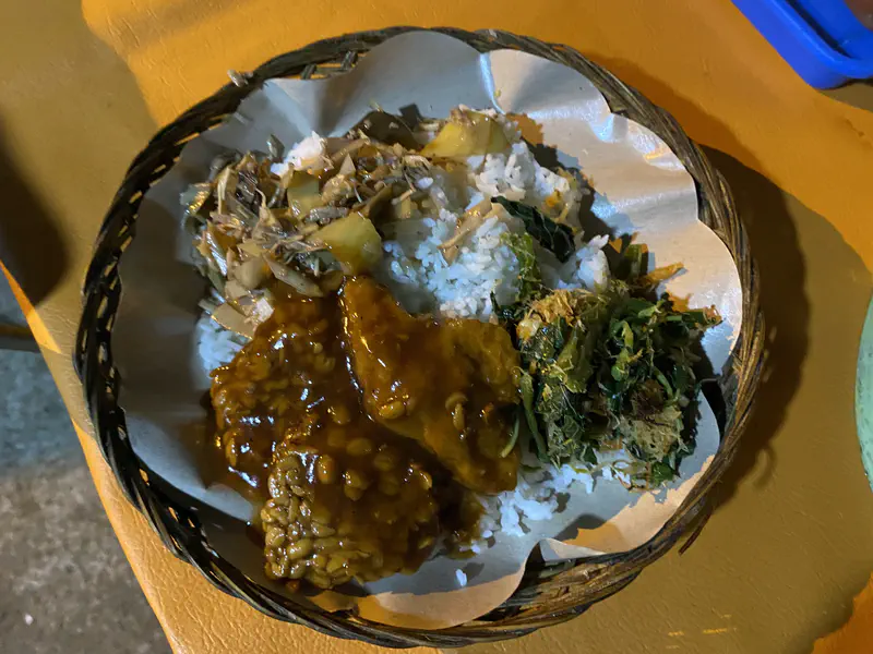 Plate of rice with tempeh in sauce, shredded vegetables, and leafy greens.
