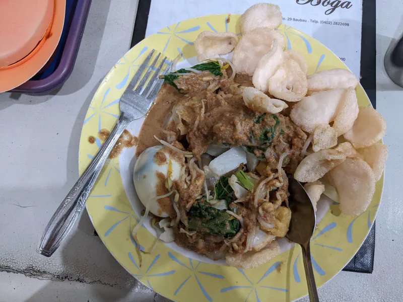 Plate of gado-gado with vegetables, egg, peanut sauce, and crackers.