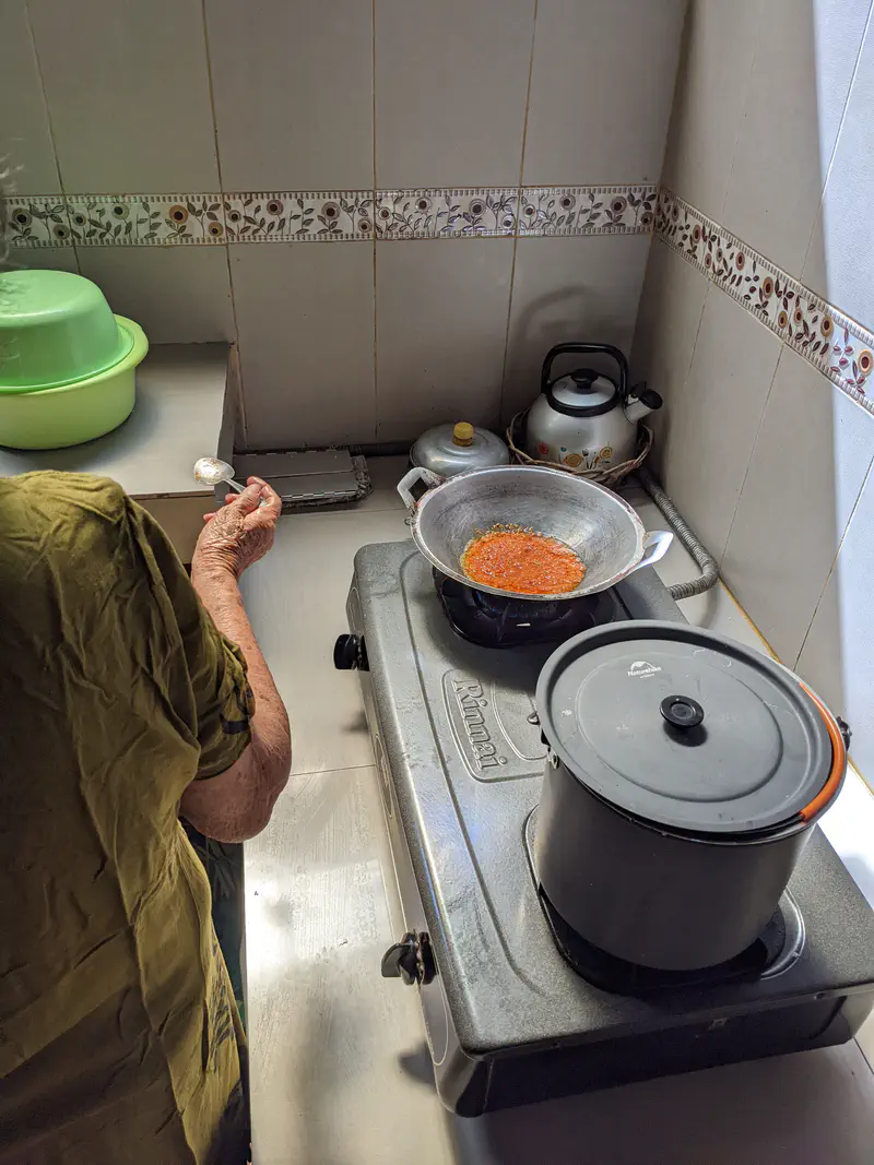Person cooking chili paste in a pan on a gas stove.