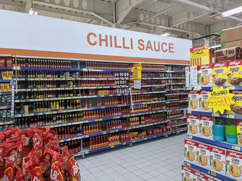 Supermarket aisle with shelves full of bottled chili sauces.