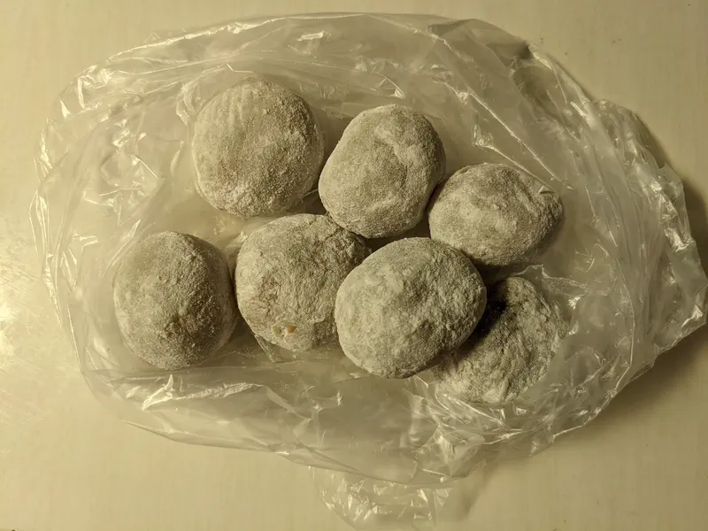 Several round mochi covered in white flour, placed inside a plastic bag on a light-colored surface.