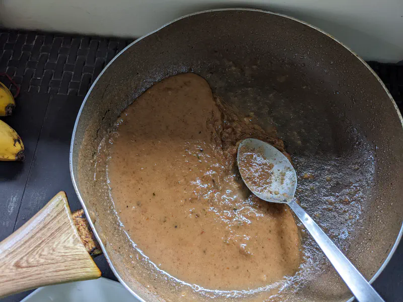 Pan with peanut sauce being stirred with a spoon.