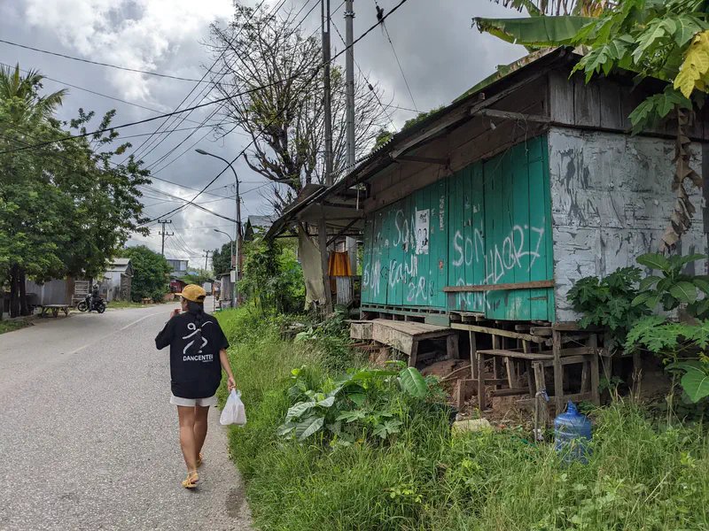 Person walking past a wooden house with graffiti on a roadside.