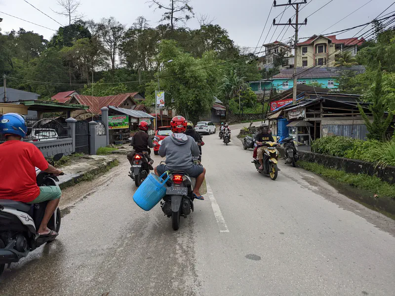 Group of motorcyclists riding through a small town, one carrying a blue basket.