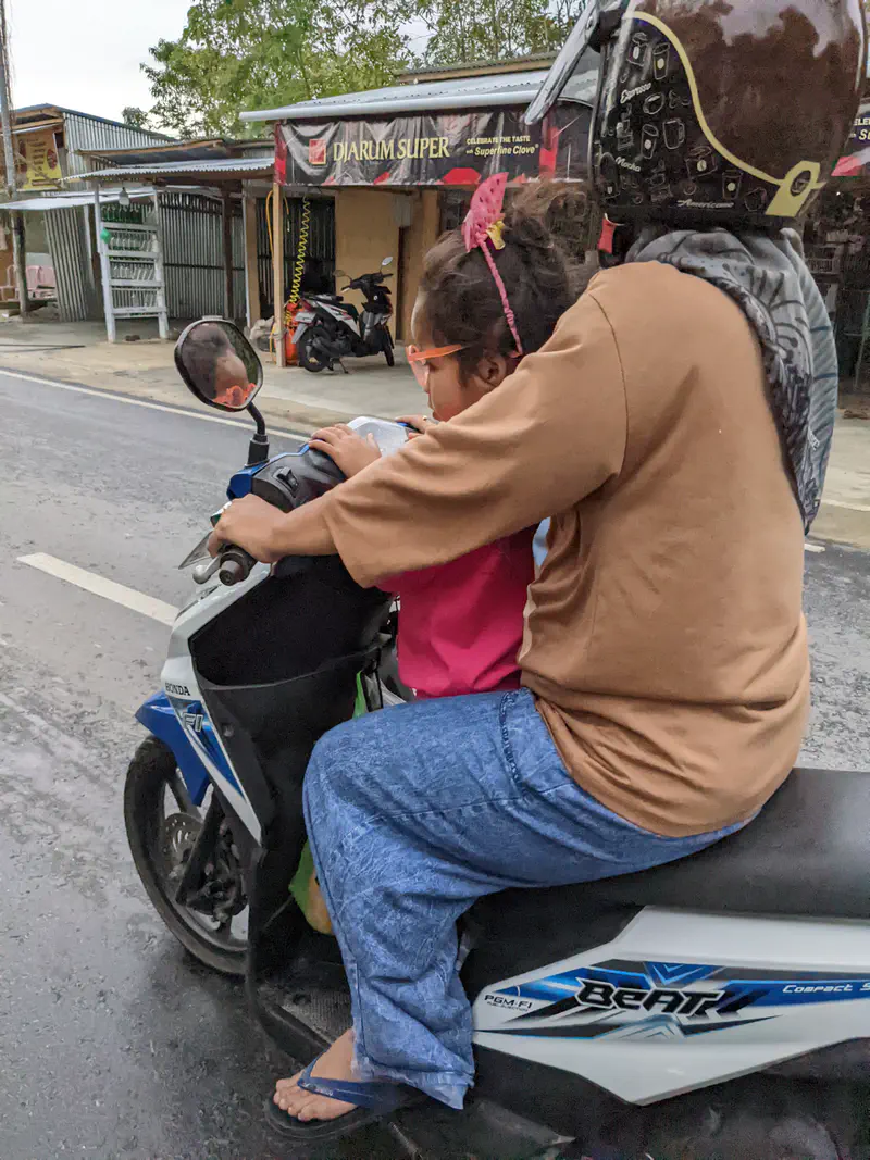 Adult riding a motorbike with a child sitting in front holding the handlebars.