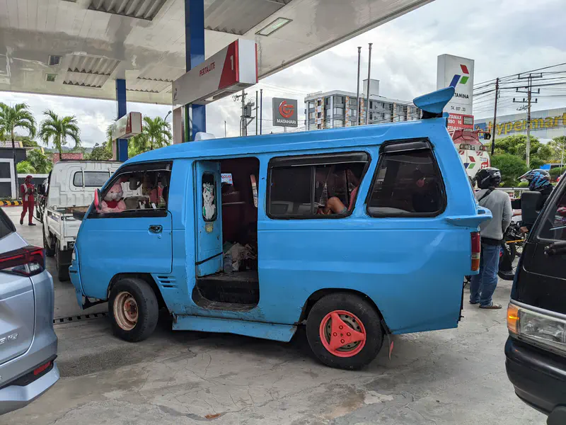 Blue minivan with red wheels parked at a gas station.