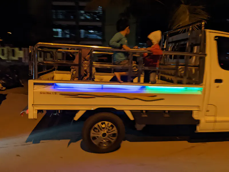 Children riding in the back of a pickup truck at night with neon lights.